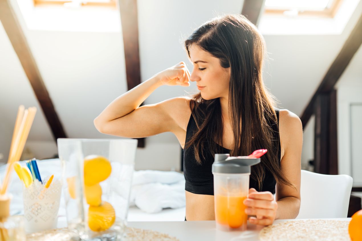 Vitamin c 1000 unterstuetzt Immunsystem und Energie – Frau mit Smoothie zeigt Bizeps in Alltagsszene