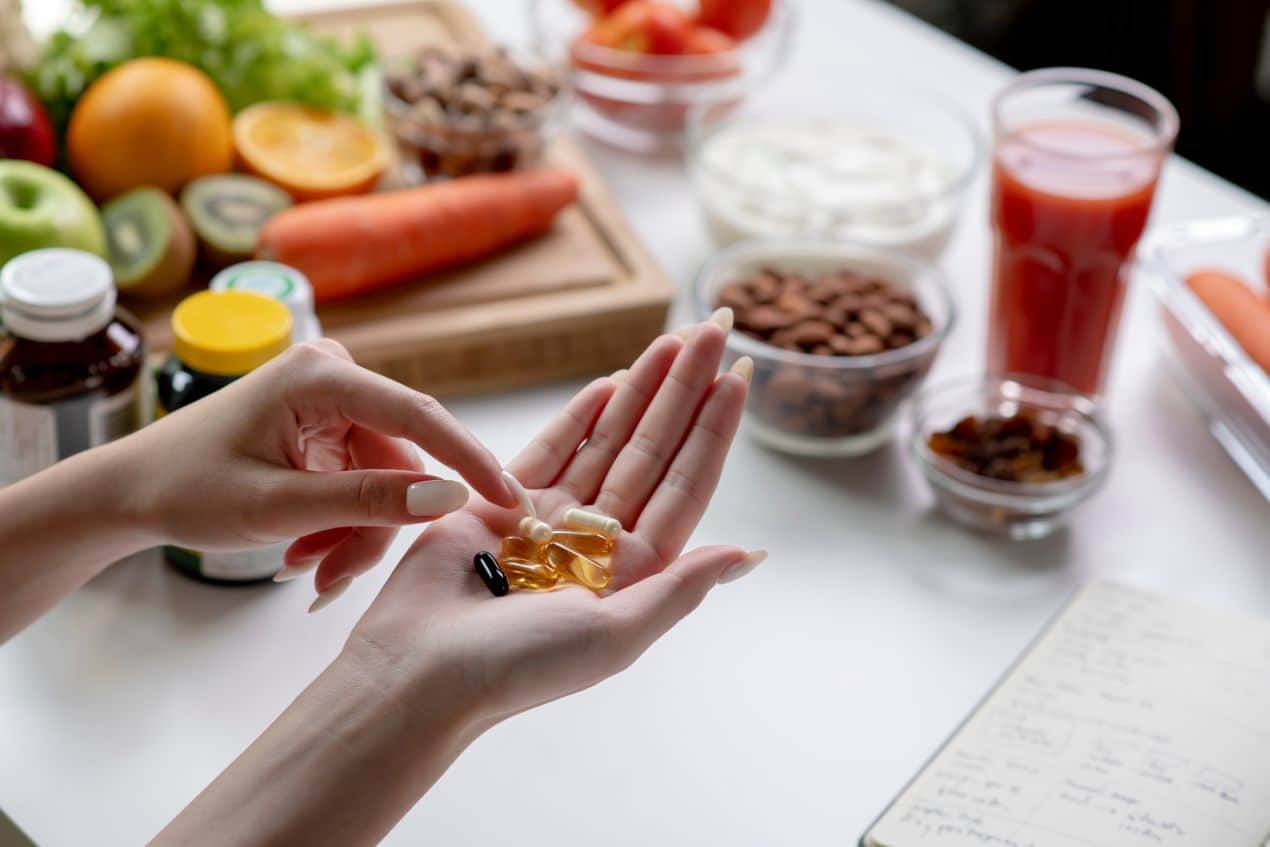 Vitamin c 1000 und Vitaminkapseln in der Hand vor Obst, Gemuese und gesunden Snacks auf dem Tisch