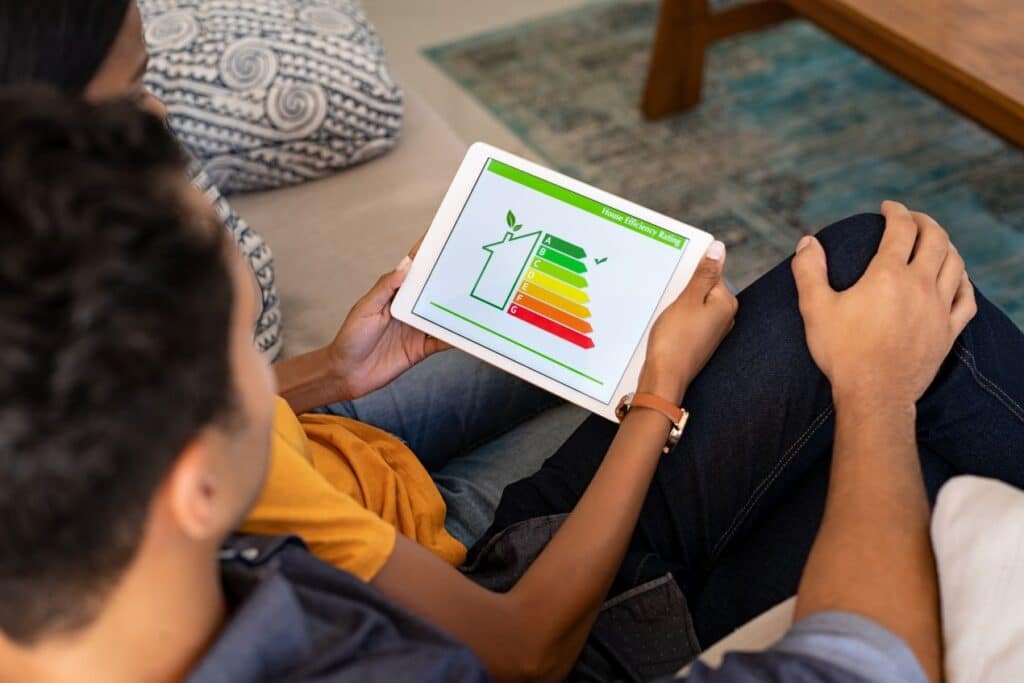 Zwei Personen sitzen auf dem Sofa und schauen auf ein Tablet mit Energieeffizienzskala – LED Einbaustrahler als Teil moderner Stromsparstrategie